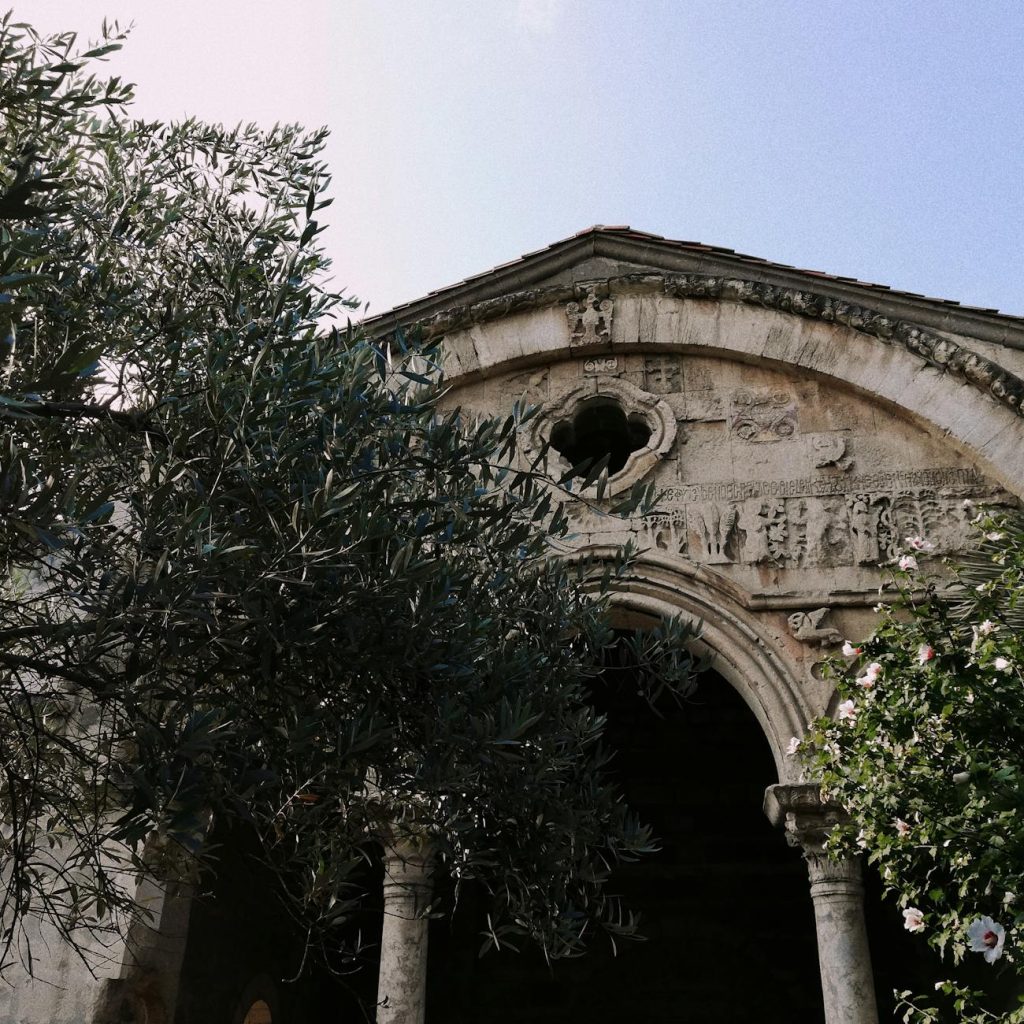 Historic church facade with intricate reliefs and arch design surrounded by lush greenery.