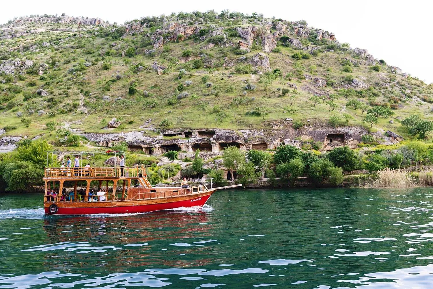 A tour boat below the rock-cut houses of Halfeti
